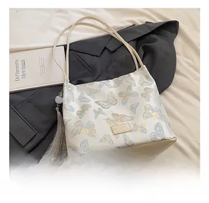 Detail of embroidered butterfly patterns on a beige bucket bag with tassel accent