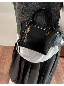 Sac seau trapèze noir brillant avec poignées en anneaux et charms sur modèle