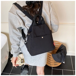 Model wearing a black multifunctional nylon backpack with top handle in a casual setting