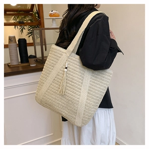 Detail of a beige woven straw tote bag with long tassel charms and wide shoulder strap