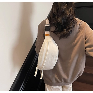 Detailed close-up of cream-white canvas waist bag with orange tag and woven zipper pulls