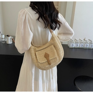 Model wearing a minimalist beige woven straw hobo bag with a leather flap and buckle