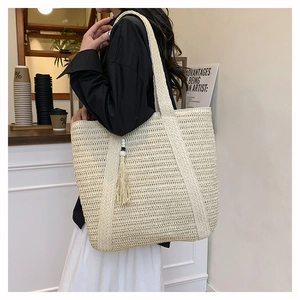 Close-up of beige woven straw tote bag with elegant tassel detail in a cafe setting