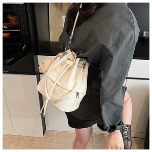 Detail of a beige drawstring bucket bag with a brown teddy bear pendant and shoulder strap