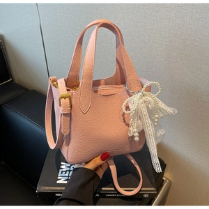 Detail of pink lychee leather handbag featuring white lace pearl bow and gold buckle