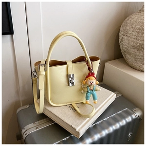 Detail of pale yellow bucket bag with metal lock and cartoon charm on a vintage book