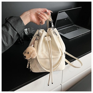 Detail of cream drawstring bucket bag with tassel and plush dog charm on a laptop desk