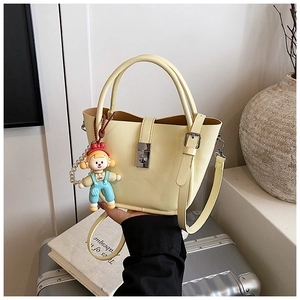 Detail of light yellow leather bucket bag with silver metal clasp and cute doll pendant