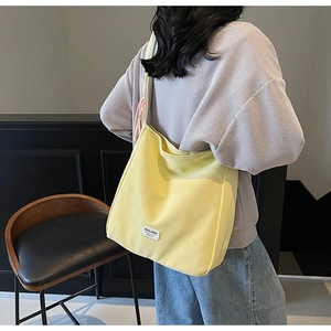 Detailed shot of yellow canvas tote bag with woven pendant and brand label on shoulder