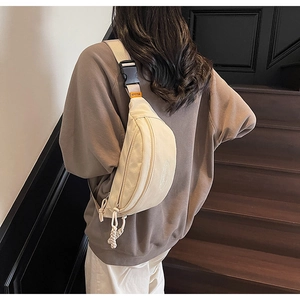 Detail of beige canvas crescent chest bag with LomMulaidi logo and orange label detail