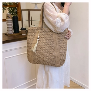 Detail of hand-woven straw tote bag featuring white long tassels and wooden bead accents