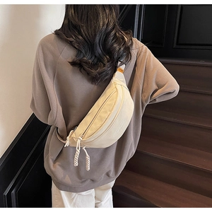 Detail of a beige crescent crossbody bag with woven rope zipper and orange label