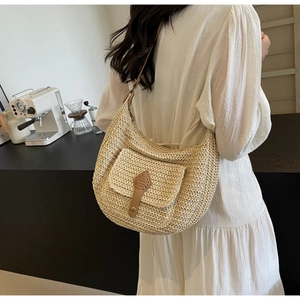 Detail showing the cream woven texture and brown leather strap of the half-moon straw bag