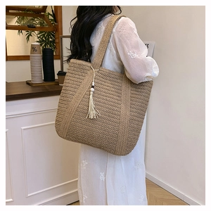 Detail of hand-woven straw tote bag featuring white fringe tassels and shoulder strap