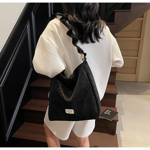 Detail of black tote bag featuring unique ruffled shoulder straps and brand label