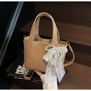 Detail of khaki pebbled leather bucket bag with white lace bow and pearl decoration