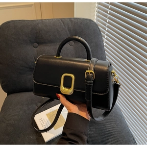 Détail du sac à main en cuir noir brillant avec fermoir doré sur un fauteuil chic