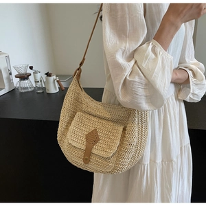 Detail of straw woven crossbody bag with brown leather strap and front flap pocket