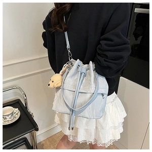 Detail of light blue drawstring bucket bag with pleated texture and plush dog pendant