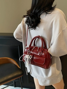 Luxury dark red Boston bag with shiny leather finish and bow detail worn by a model