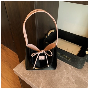 Détail du sac seau en cuir verni noir avec ruban rose et étiquette logo en cuir
