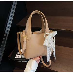 Detail of beige lychee leather bucket bag featuring a lace pearl bow and gold hardware