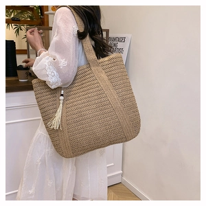 Detailed texture of a large beige straw tote bag with white tassels on a shoulder strap