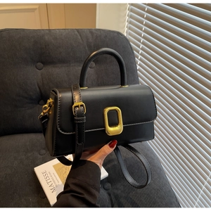 Vue détaillée d'un sac à main en cuir noir avec boucle dorée sur un canapé gris