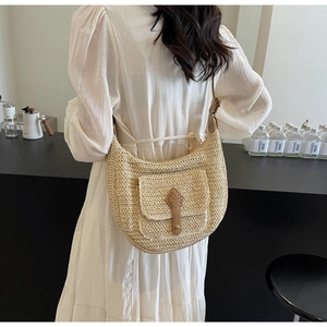 Close-up of a large straw crescent bag with brown leather strap and front pocket detail