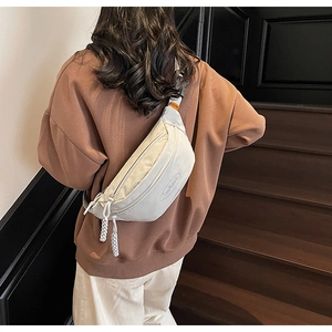 Detail of light grey nylon chest bag worn on back with woven zipper pullers