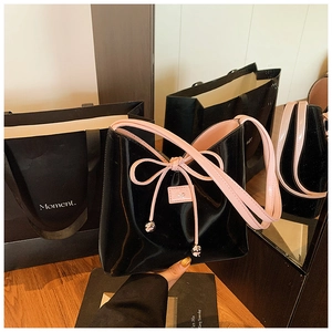 Détail du sac seau en cuir verni noir brillant avec nœud rose et breloques en métal