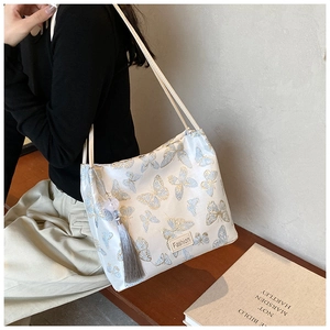 Close-up of embroidered butterfly patterns and grey tassel on a white bucket bag