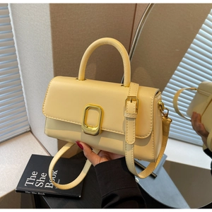 Détail d'un sac à main carré minimaliste crème avec boucle dorée et poignée ronde