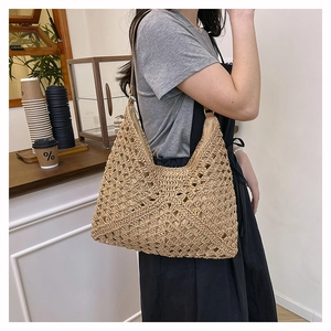 Detail of hand-woven beige straw hobo bag with slim leather straps in a cafe setting