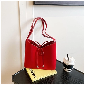 Détail du sac bandoulière en cuir verni rouge avec nœud et perles argentées sur table noire