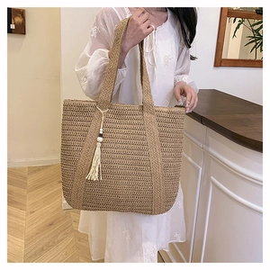 Detail view of woven straw tote bag featuring decorative white tassels and long shoulder straps