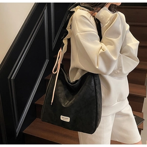 Close-up of black leather tote bag with brand logo and pink cord detail in lifestyle scene