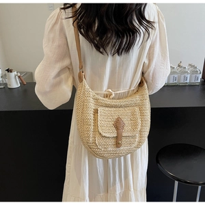 Detail of a straw shoulder bag with a brown leather buckle and slim strap on a model