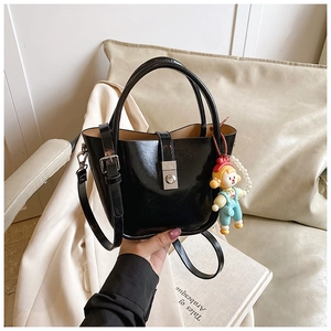 Close-up of black patent leather bucket bag with metal buckle and cute bear charm