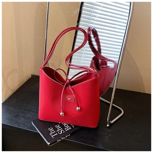 Détail du sac seau rouge avec nœud en cuir à cordon et pendentifs en boules de métal