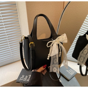 Detail of black lychee leather bucket bag with white lace bow and pearl charm