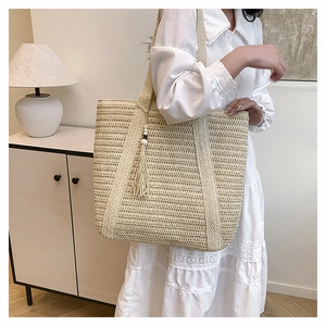 Detail of the woven straw tote bag featuring tassel charms and fine handcrafted textures