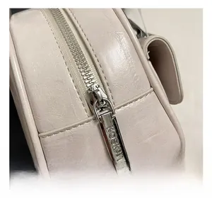 Close-up of silver metal zipper pull with engraved KOSK logo on beige leather bowling bag