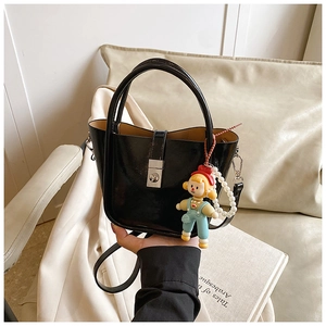 Detail of black glossy patent leather bucket bag with pearl doll charm and metal clasp