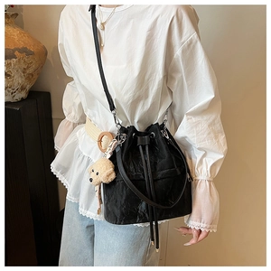 Fashionable black drawstring bucket bag with a cute dog pendant and textured fabric details