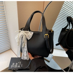 Detail of black lychee leather bucket bag with white lace bow and pearl charms