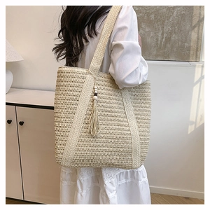 Detail of a large cream woven straw tote bag featuring parallel straps and tassel charm