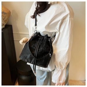 Detail of black drawstring bucket bag with pleated texture and soft pompom pendant