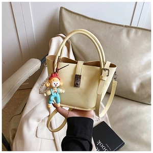 Detail view of cream bucket bag featuring silver twist lock and cute doll charm accessory