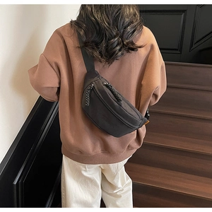 Detailed view of the black canvas chest bag with orange tag and dual zipper pulls